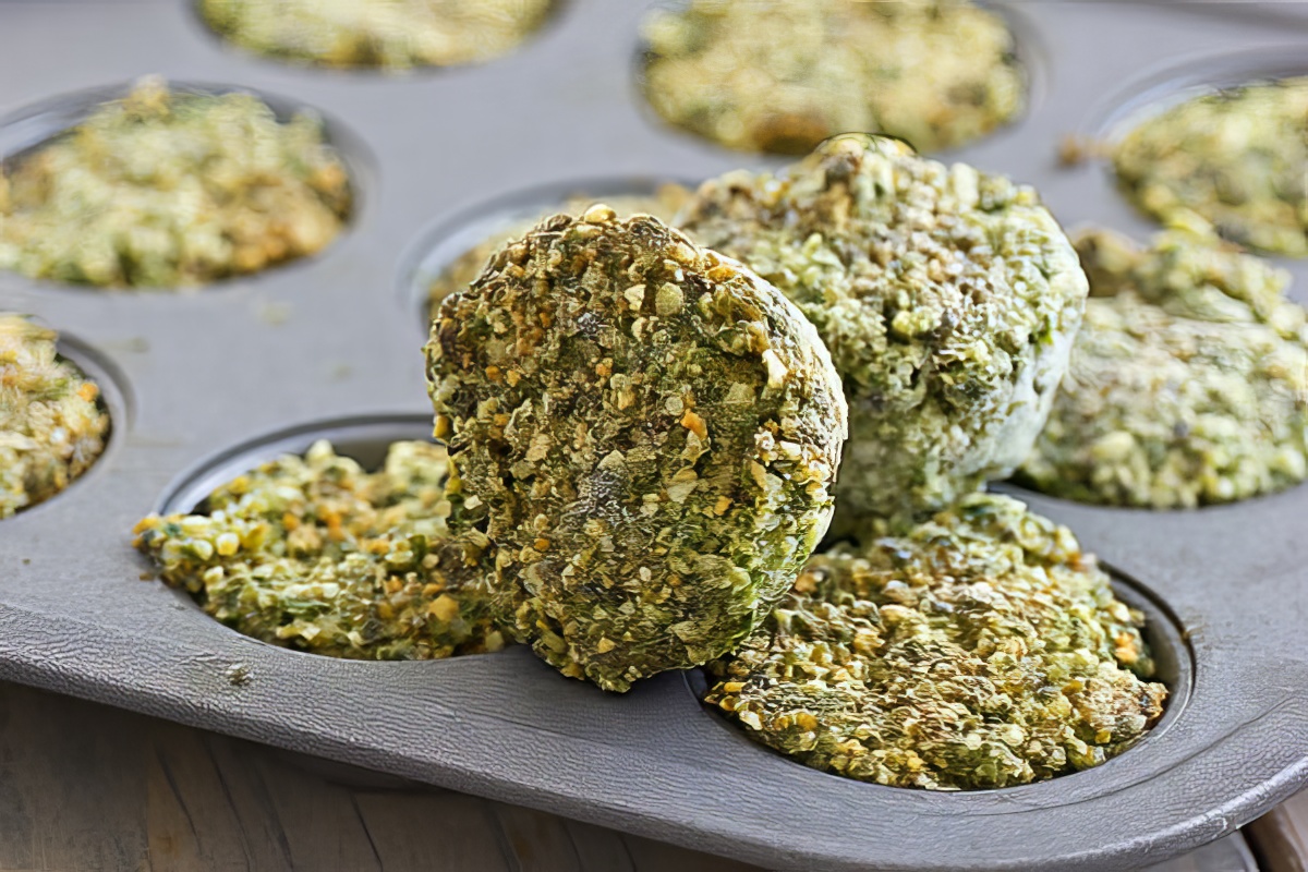 An ice cube tray filled with frozen portions of spinach pesto on a kitchen counter, with a few cubes popped out nearby