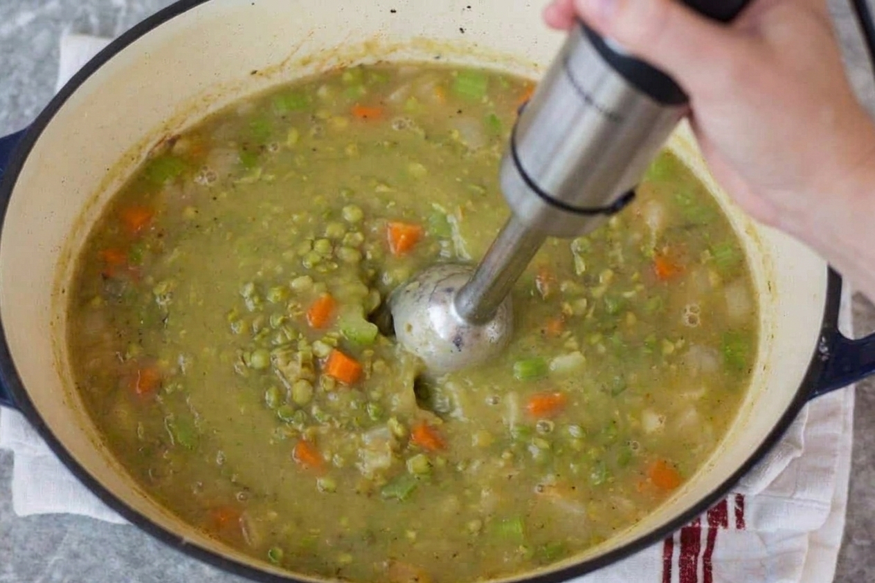An immersion blender partially blending split pea soup inside a pot