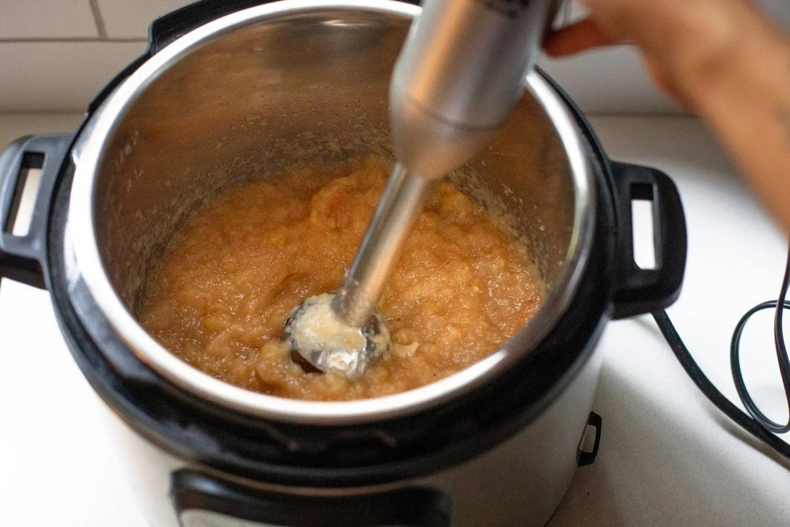 An immersion blender pureeing soft cooked apples in a large pot on a stovetop, with steam rising