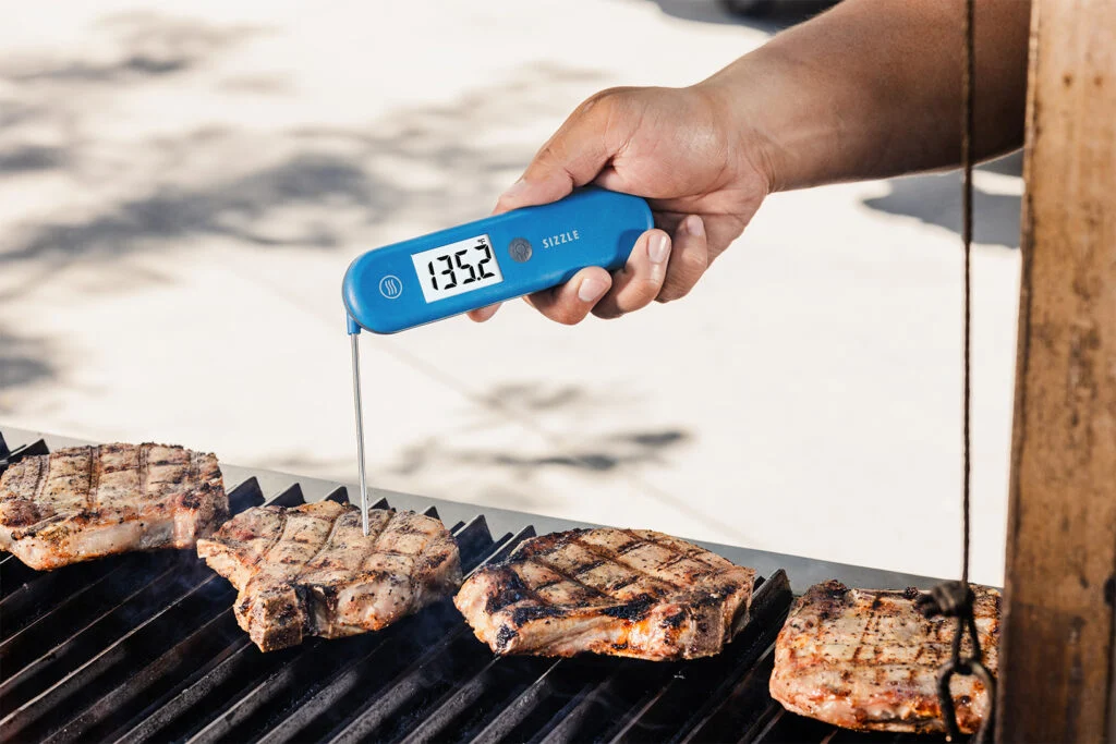 An instant-read meat thermometer inserted into the thickest part of a baked pork loin chop on a sheet pan in a home kitchen