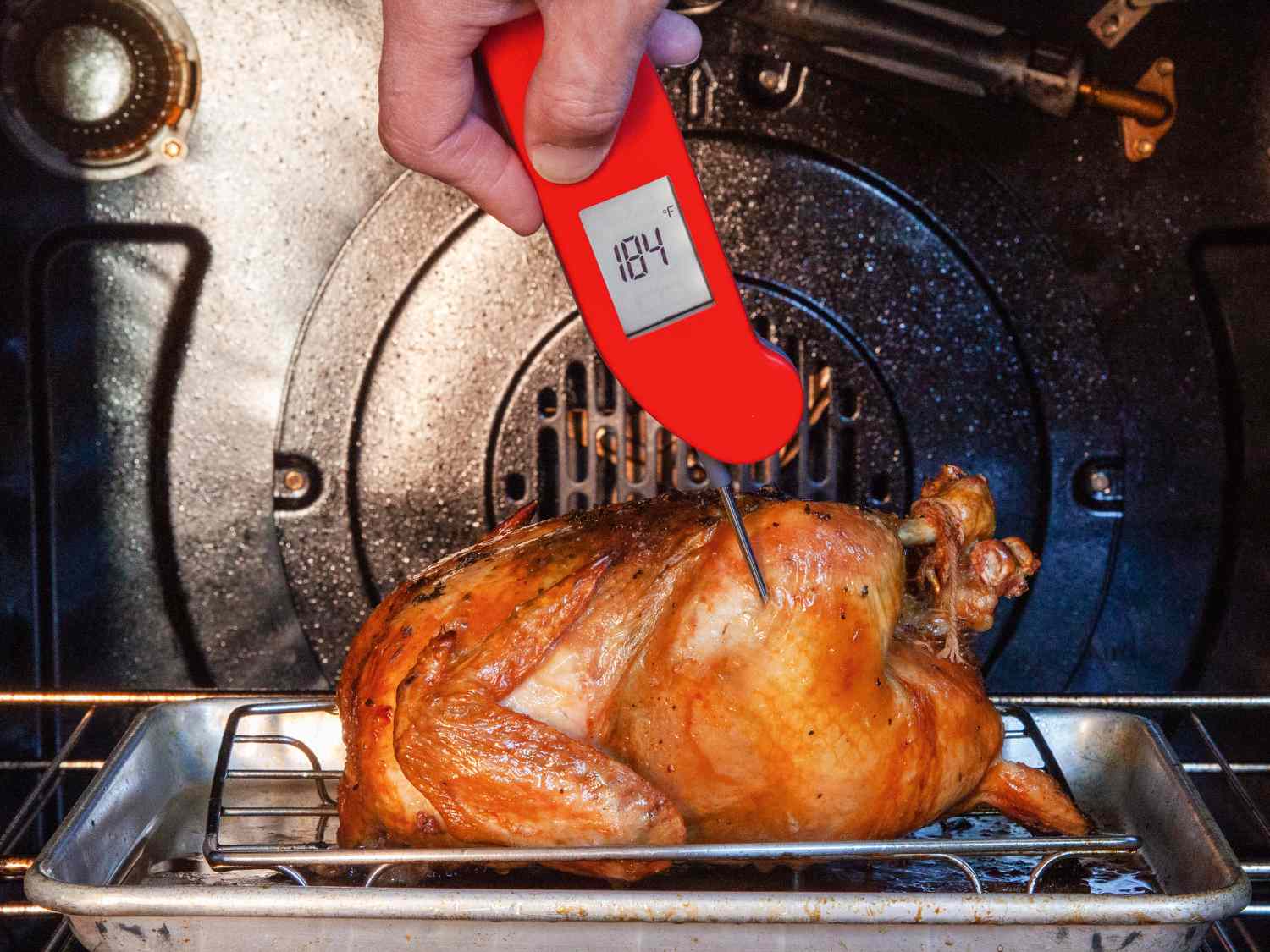 An instant-read thermometer being inserted into a thick piece of chicken in a skillet to check doneness