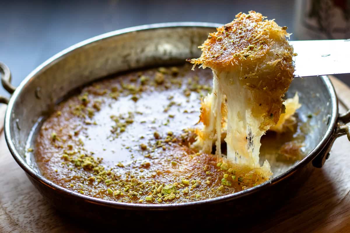 An oven-safe skillet on a stovetop next to a saucepan of syrup, set up on a tidy kitchen counter with warm lighting