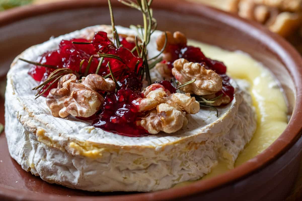 An unbaked wheel of brie centered in a small white ceramic baking dish on a light kitchen counter