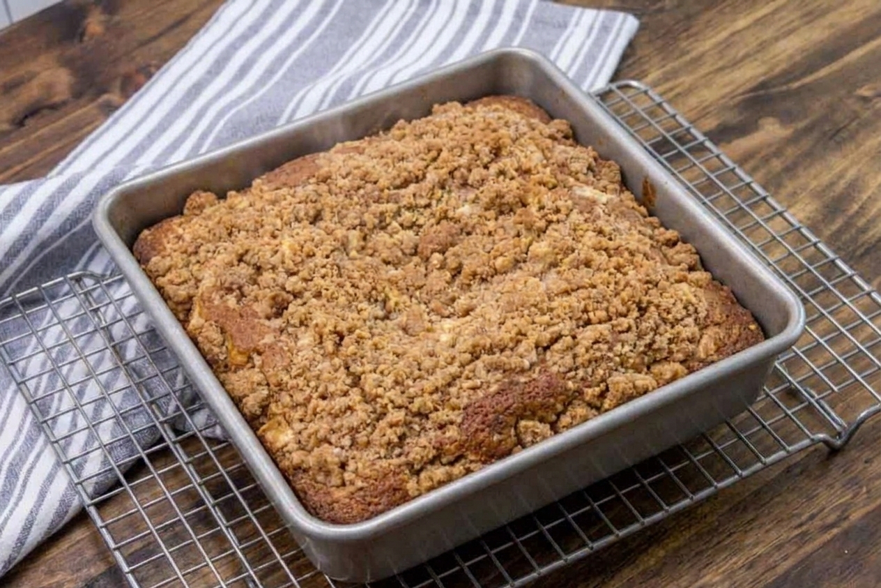 An uncut apple coffee cake with cinnamon streusel topping in a square baking pan, just pulled from the oven and set on a cooling rack