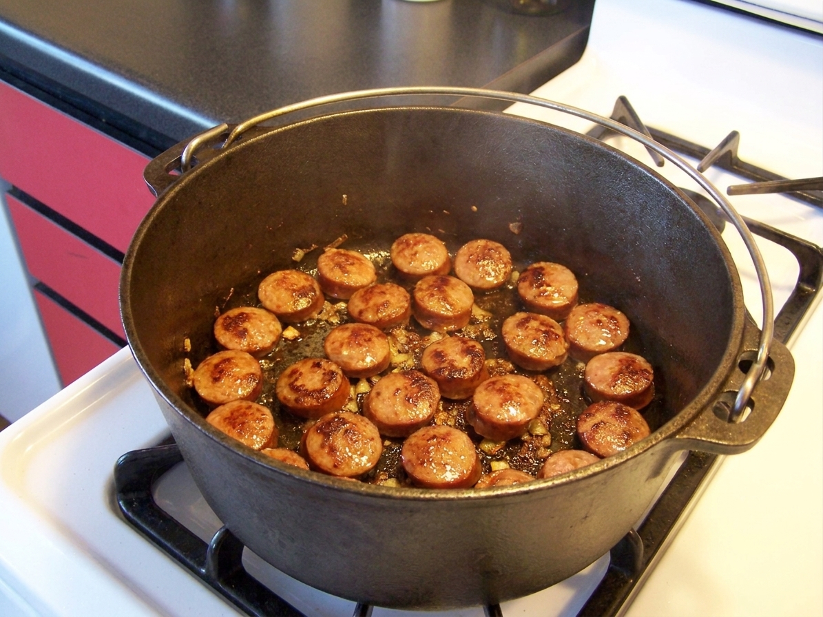 Andouille sausage rounds browning in a Dutch oven on a stovetop, with caramelized edges forming