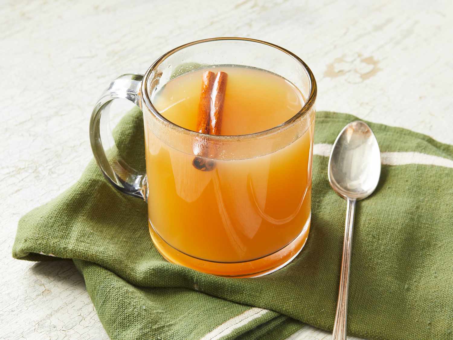 Apple cider, apple juice, sugar, cinnamon sticks, cloves, star anise, and vanilla arranged on a kitchen counter