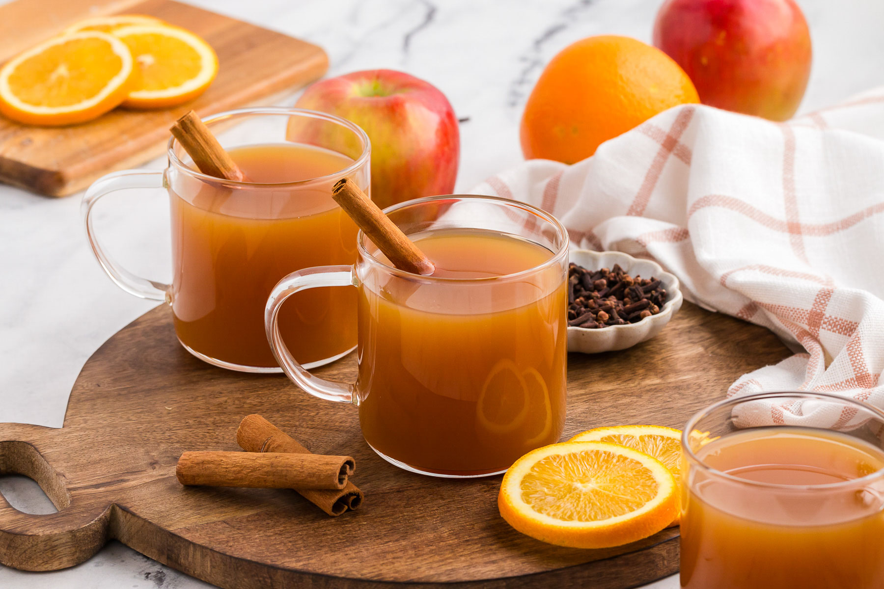 Apple cider in a glass bottle with orange slices, cinnamon sticks, cloves, and allspice on a kitchen counter