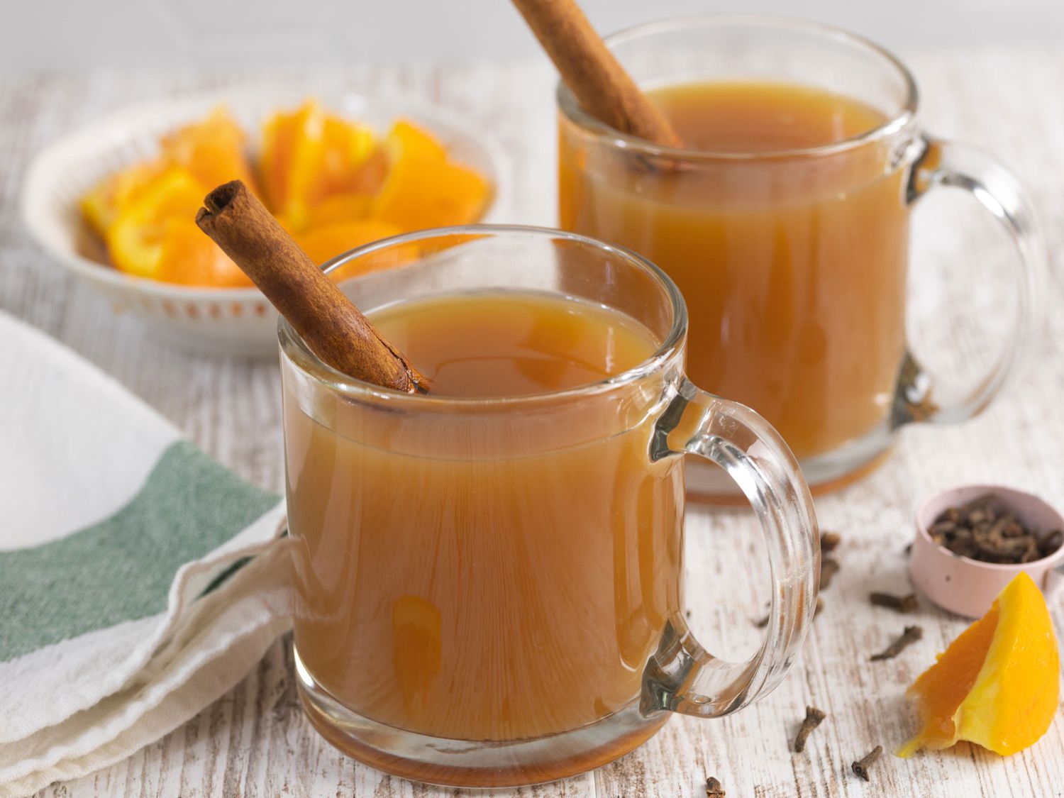 Apple cider steaming in a small saucepan with cinnamon sticks while warming on a stovetop