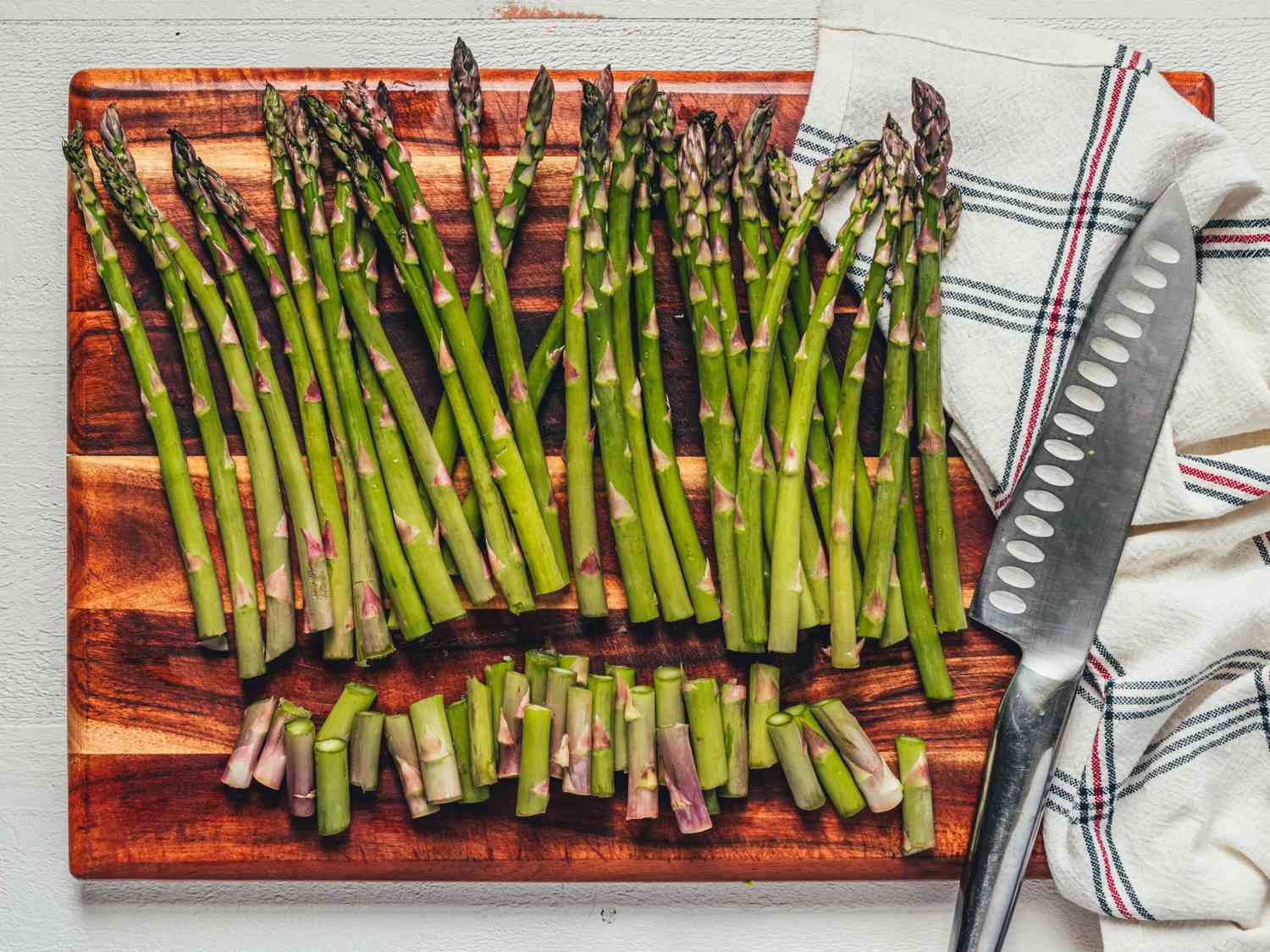 Asparagus spears lined up on a wooden cutting board with the woody ends trimmed off, kitchen knife resting nearby