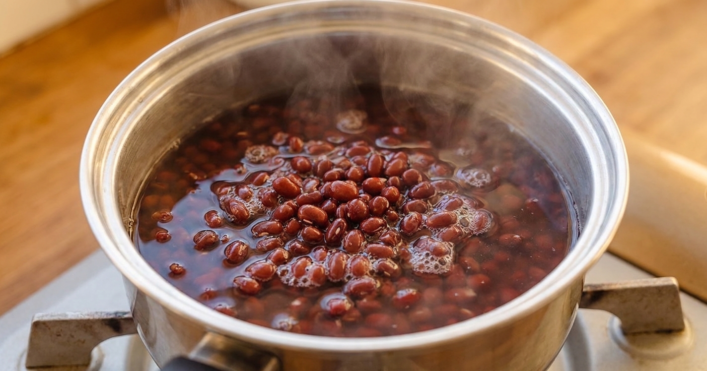 Azuki beans simmering gently in a stainless steel pot on a stovetop with steam rising