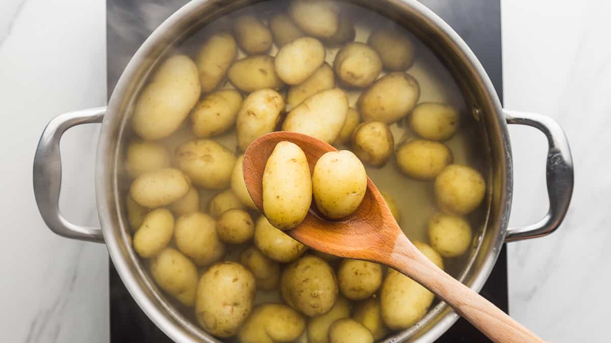 Baby potatoes simmering in a large pot of salted water on a stovetop with gentle bubbles