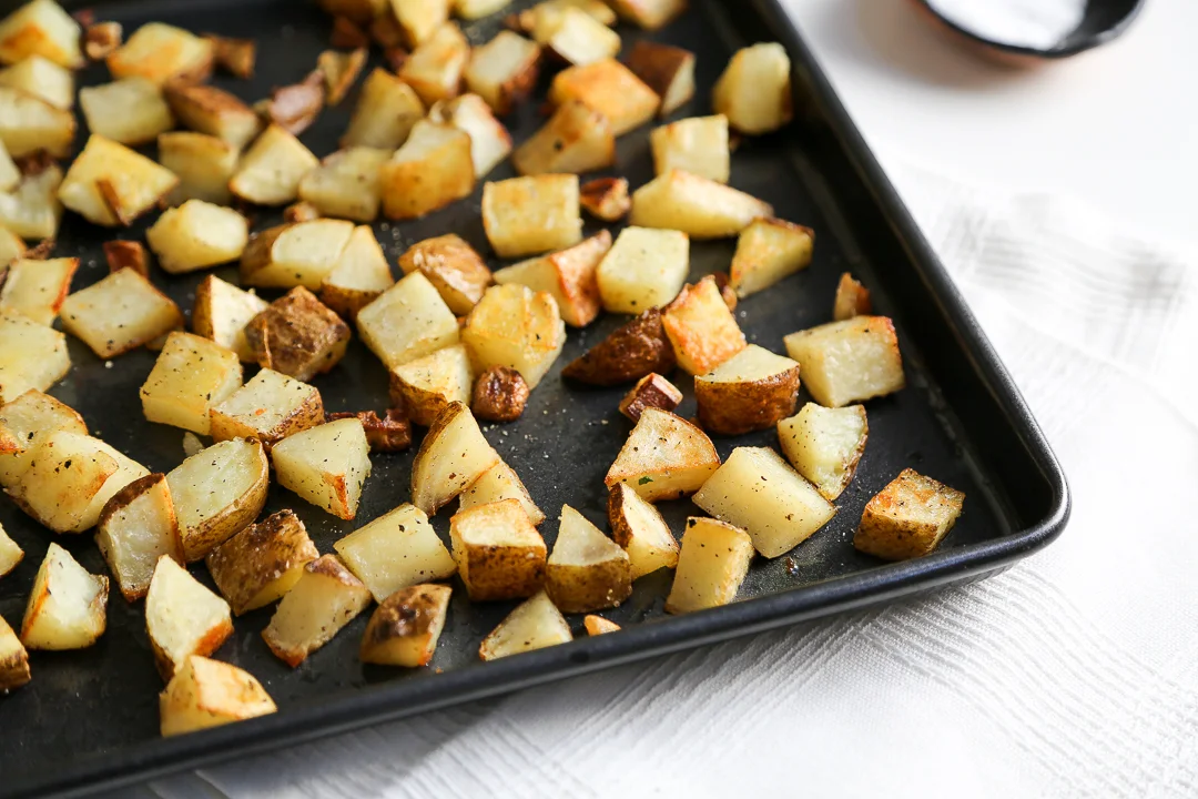 Baby potatoes spread cut-side down on a rimmed sheet pan ready to roast in a home kitchen