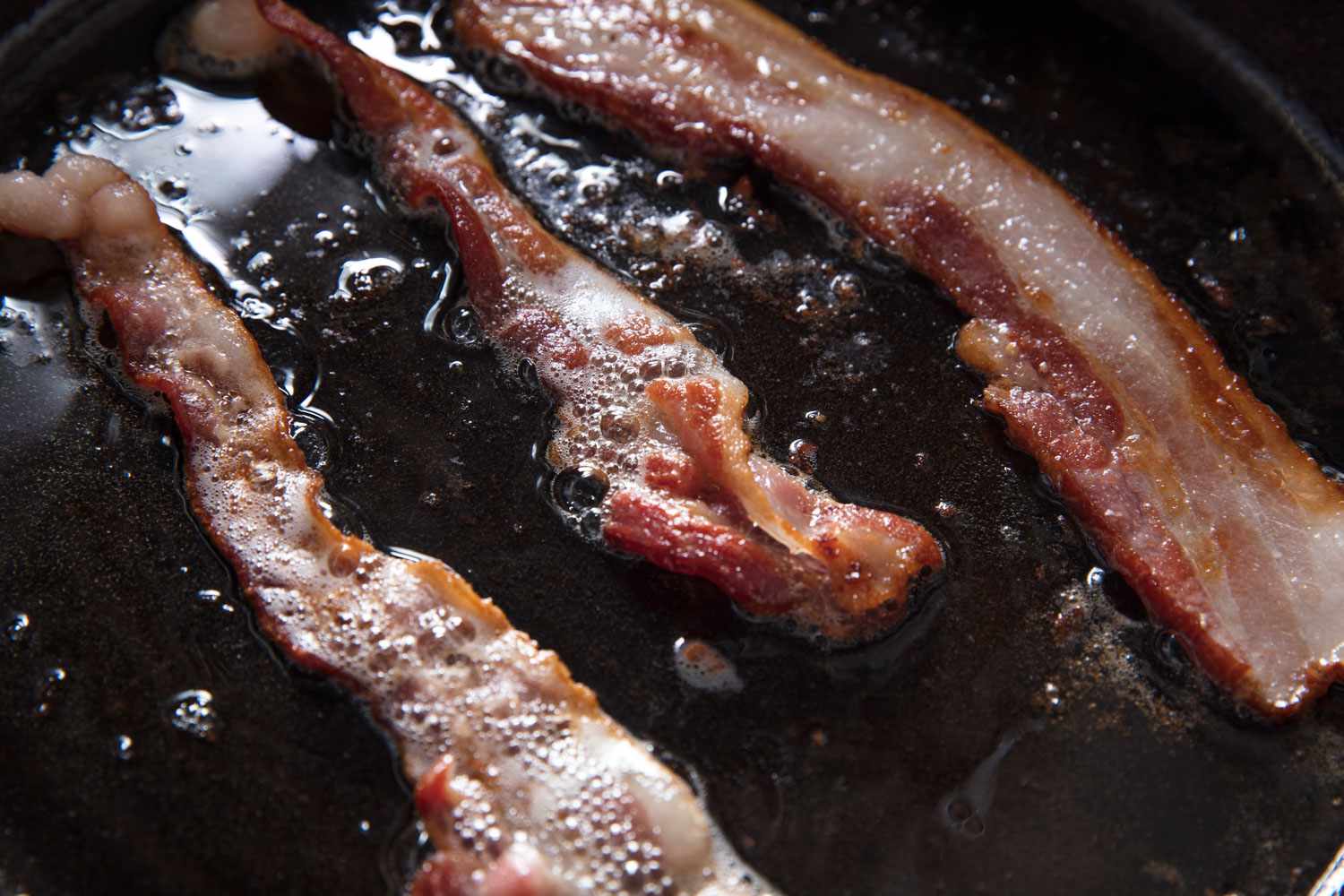 Bacon strips sizzling in a cast iron skillet on a stovetop