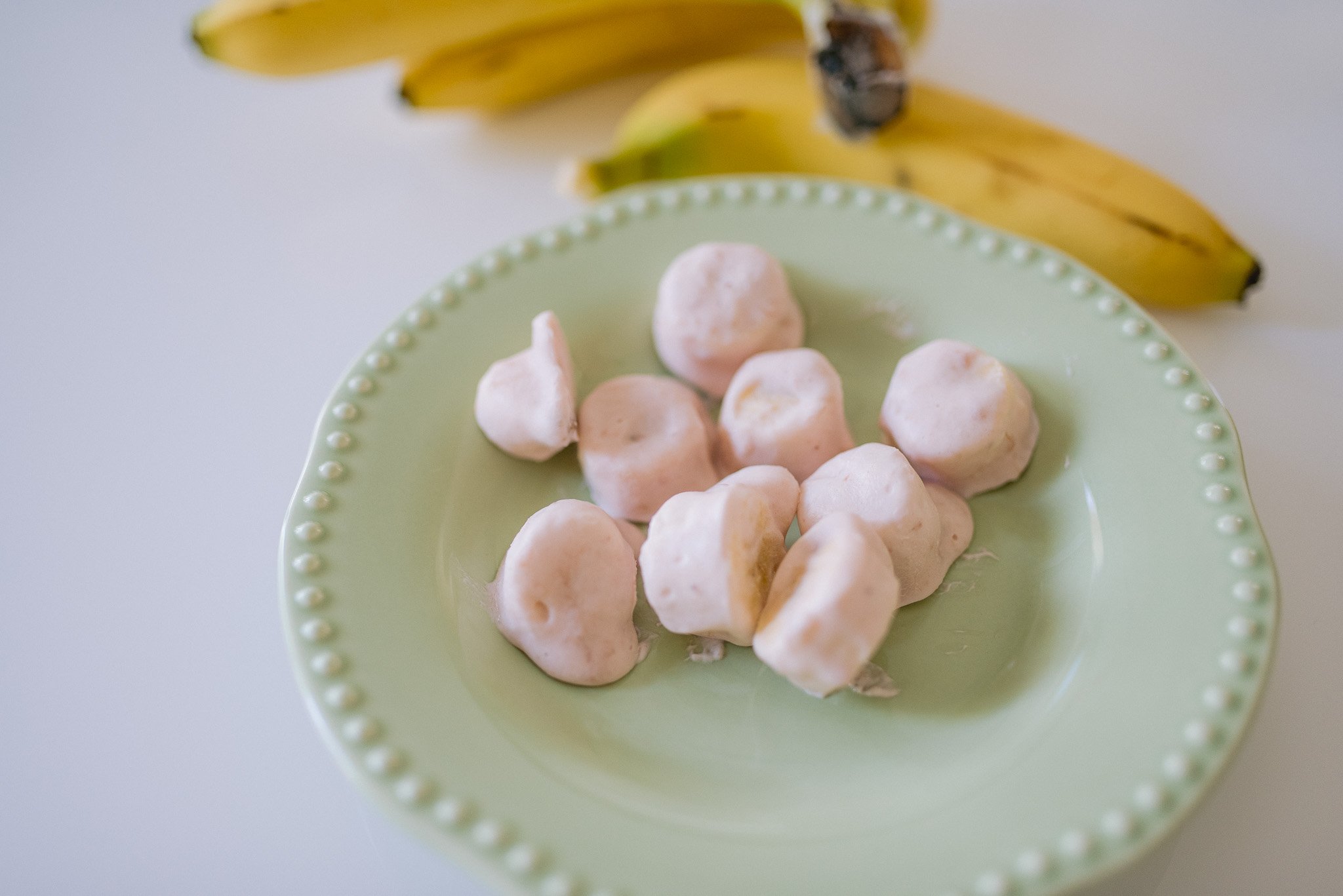 Banana slices spaced out on a parchment-lined baking sheet, ready to go into the freezer on a bright kitchen counter