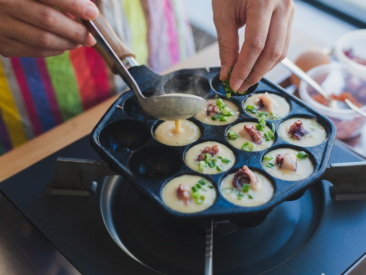 Batter being poured into a hot takoyaki pan while octopus pieces and green onions are added
