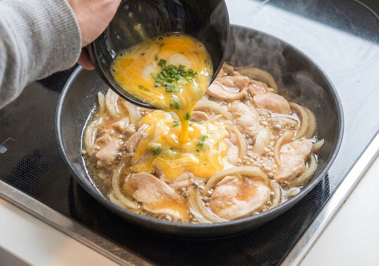 Beaten egg drizzled over simmered chicken and onions in a skillet, with the egg beginning to set into soft ribbons
