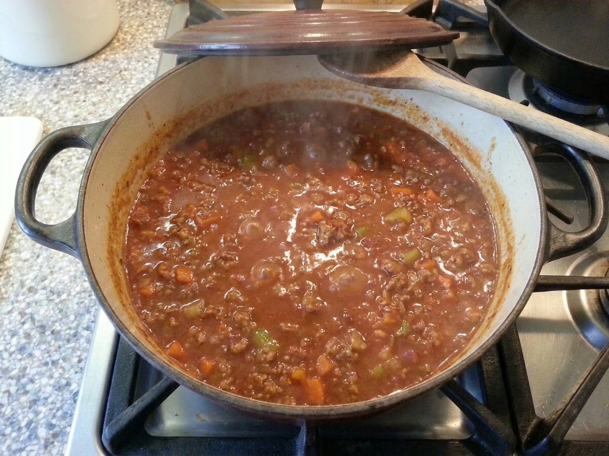 Beef bolognese gently simmering in a Dutch oven with the lid slightly ajar on a stovetop