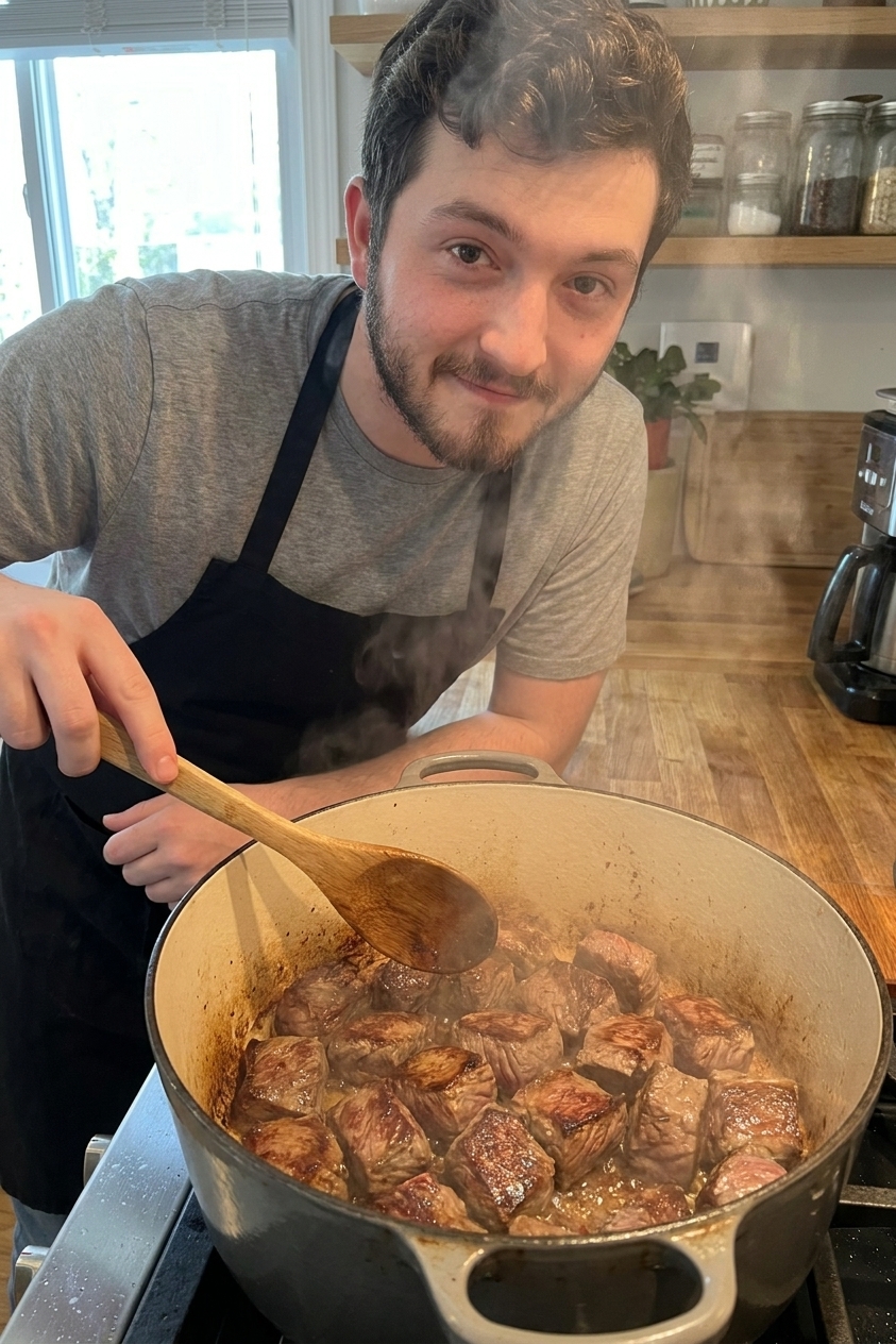 Beef cubes browning in a Dutch oven with caramelized edges and steam rising