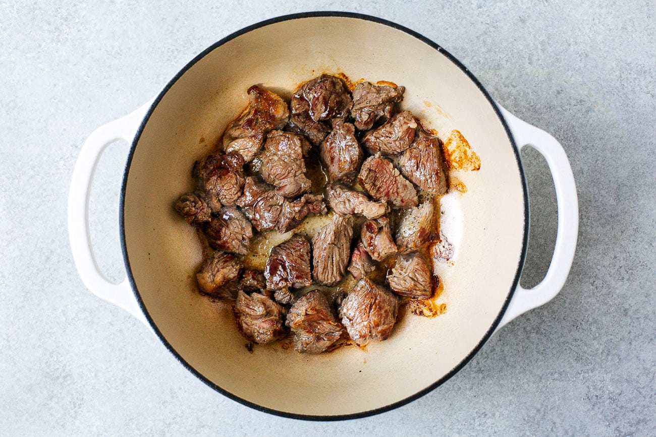 Beef cubes browning in a Dutch oven with deep caramelized edges on a stovetop