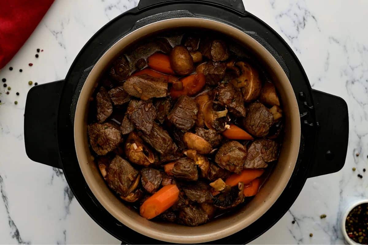 Beef cubes browning in an Instant Pot insert on sauté mode with browned bits forming on the bottom of the pot