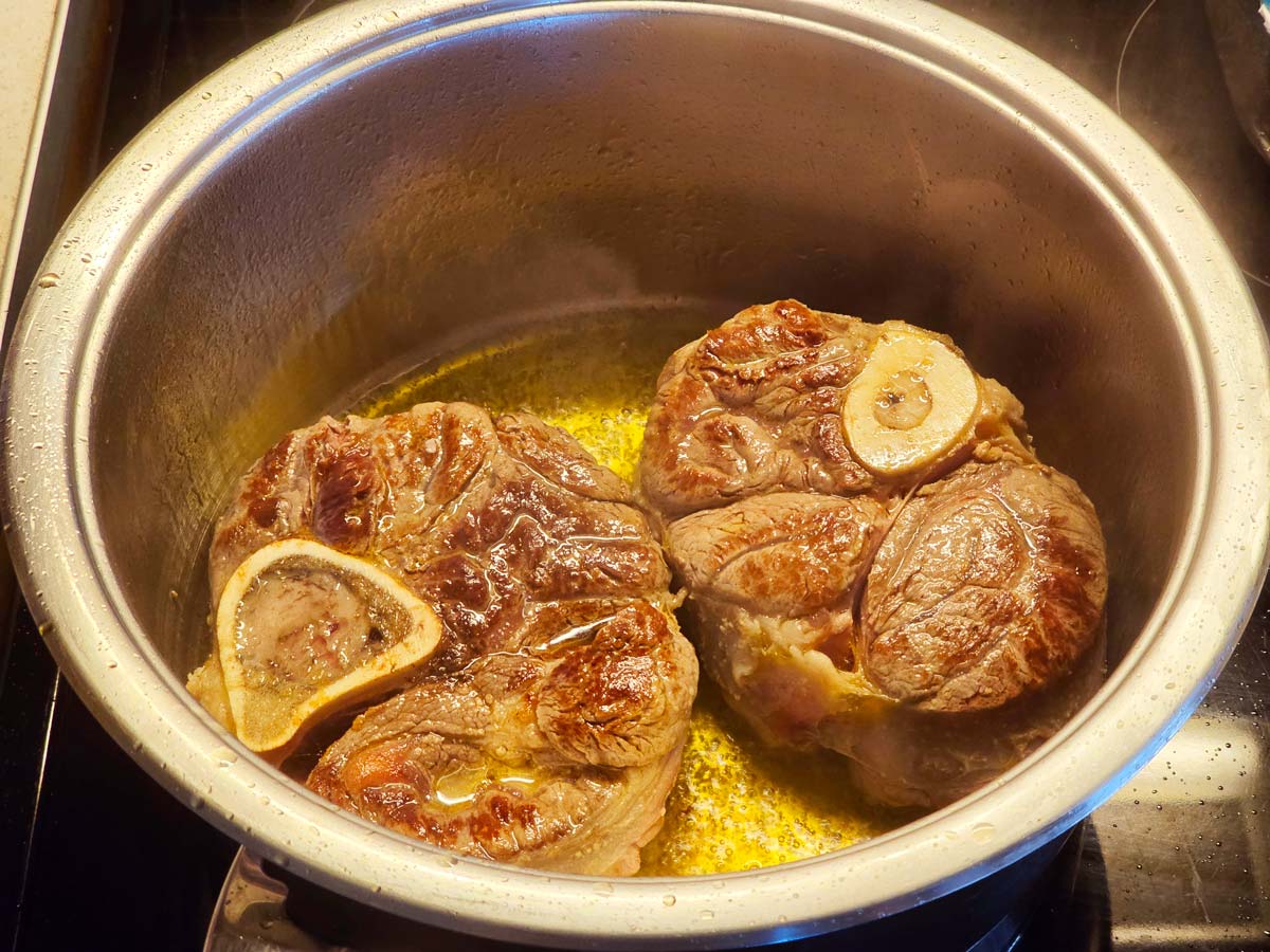Beef shank pieces simmering in a large pot with onion and bay leaves, light steam rising on a home stove