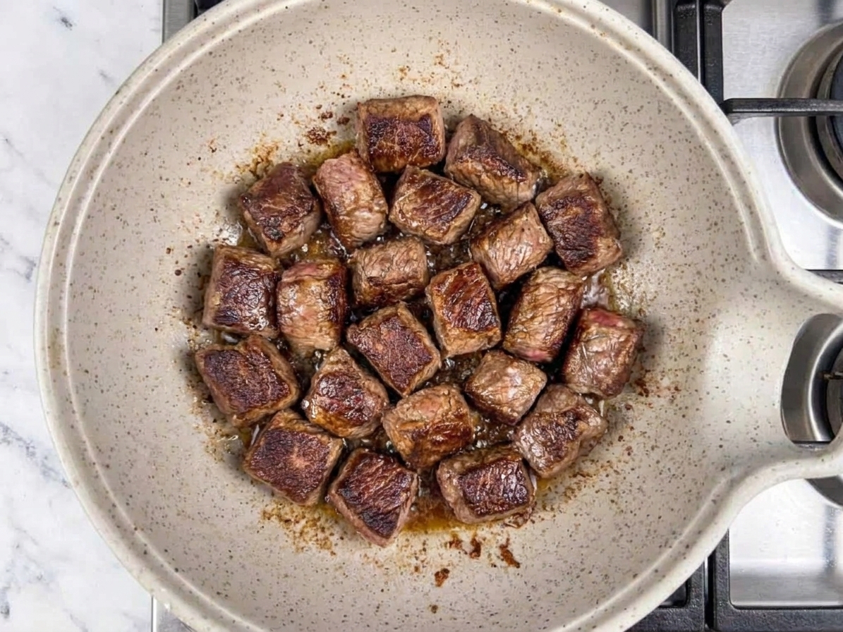 Beef stew chunks browning in a Dutch oven with caramelized edges, viewed from above on a stovetop