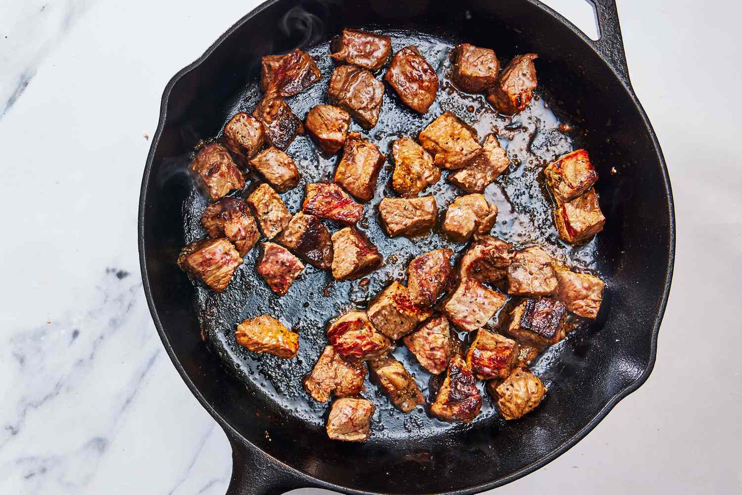 Beef tips browning in a hot skillet with visible caramelized edges and a wooden spoon nearby