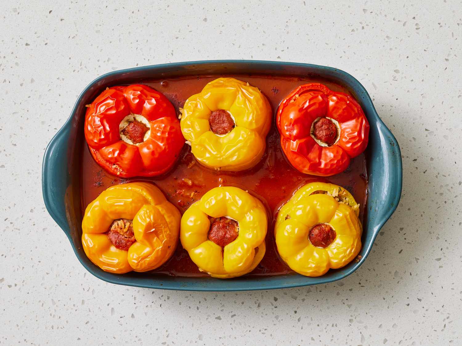 Bell peppers with tops removed and seeds cleaned out, arranged open-side up on a cutting board beside chopped pepper tops