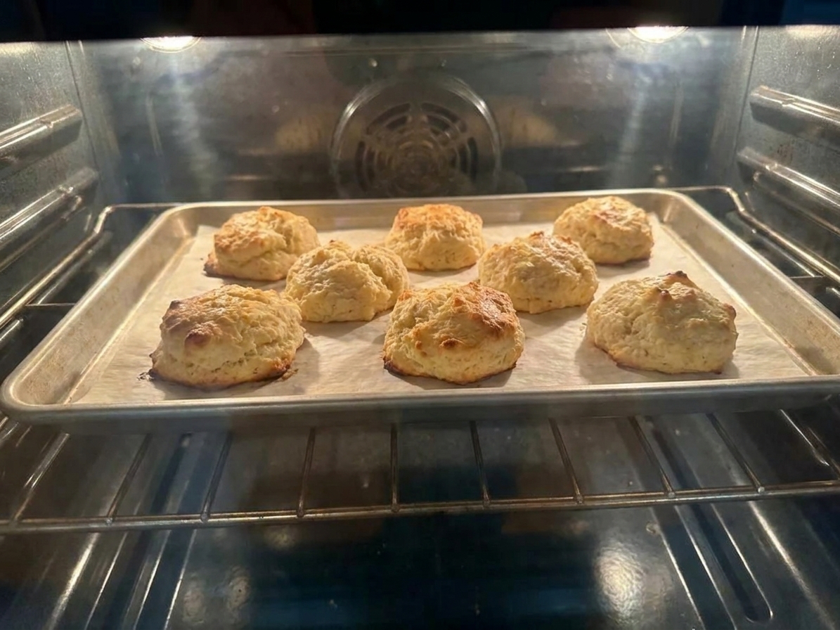Biscuits baking on a parchment-lined sheet pan inside an oven with tops turning golden