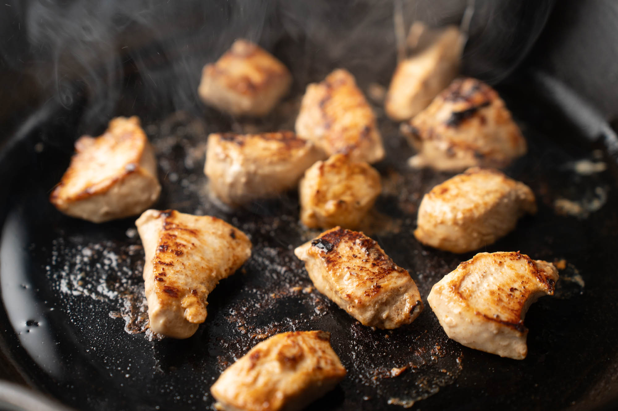 Bite-size chicken pieces searing in a hot skillet with golden browned edges on a stovetop
