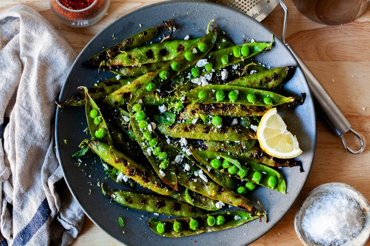Blistered sugar snap peas with browned spots and a light glossy sauce pooled slightly in a dark skillet