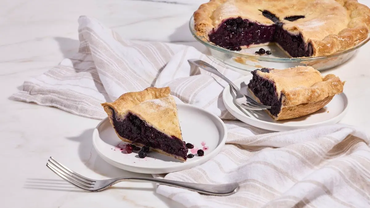 Blueberries, sugar, cornstarch, a lemon, and salt arranged on a kitchen counter with measuring spoons