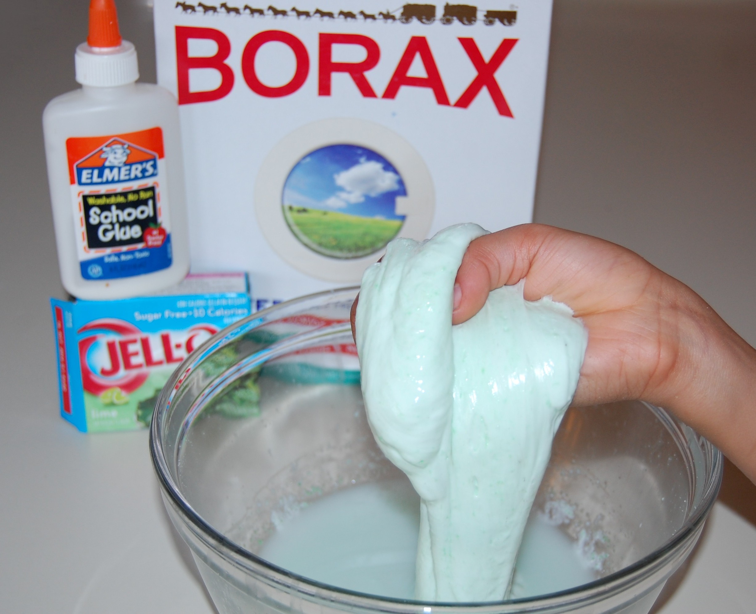 Bottles of white school glue, borax, and measuring tools set out on a bright kitchen counter for making slime