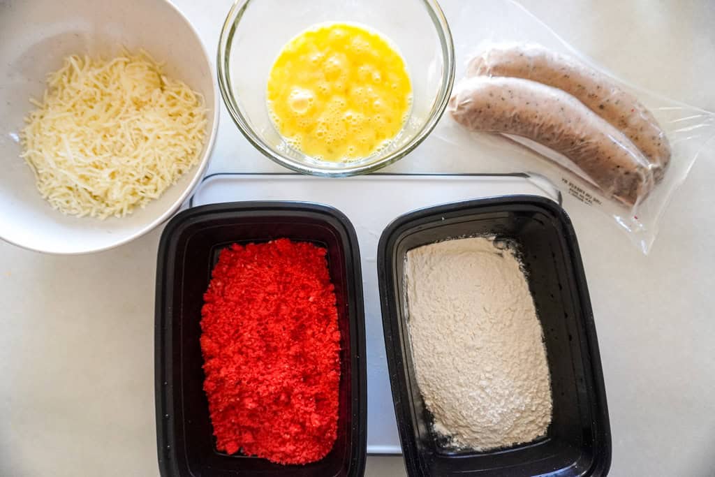 Boudin sausage links, eggs, flour, panko breadcrumbs, green onions, hot sauce, and a small bowl of Cajun seasoning arranged on a kitchen counter
