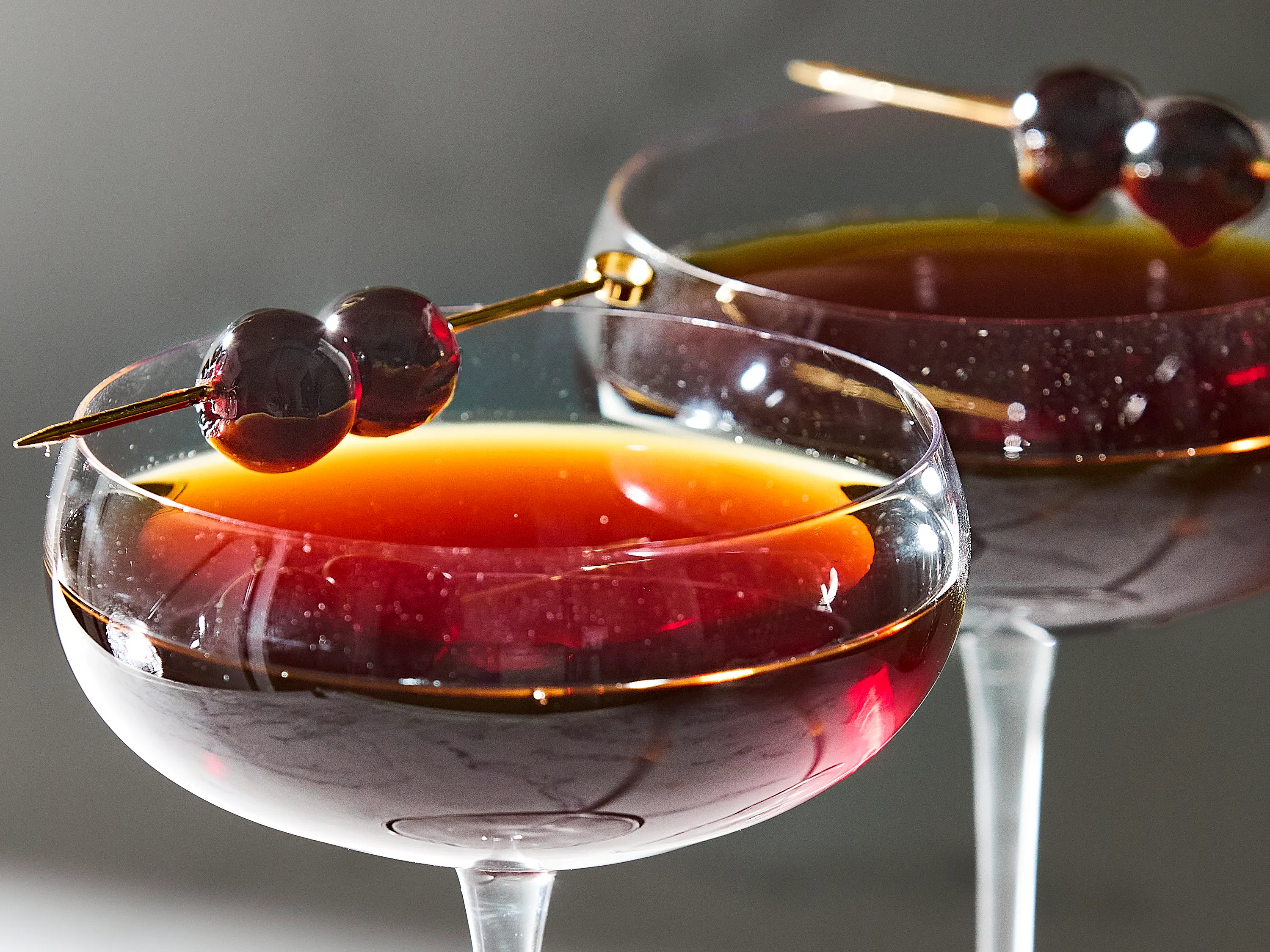 Bourbon, amaro bottle, bitters, cocktail cherries, a jigger, and a mixing glass arranged on a tidy kitchen counter under warm lighting