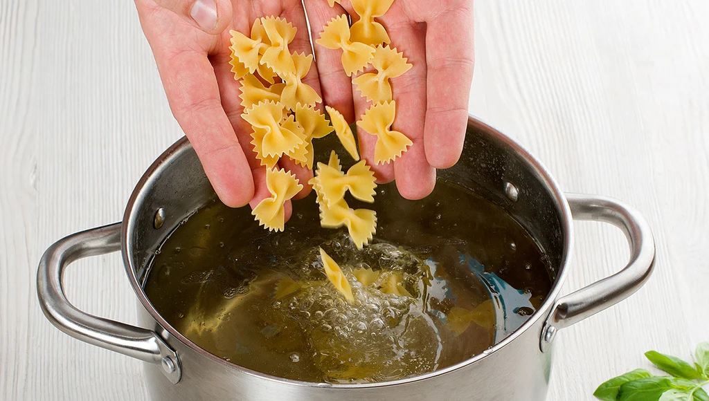 Bow tie pasta boiling in a large pot of salted water on a stovetop with steam rising