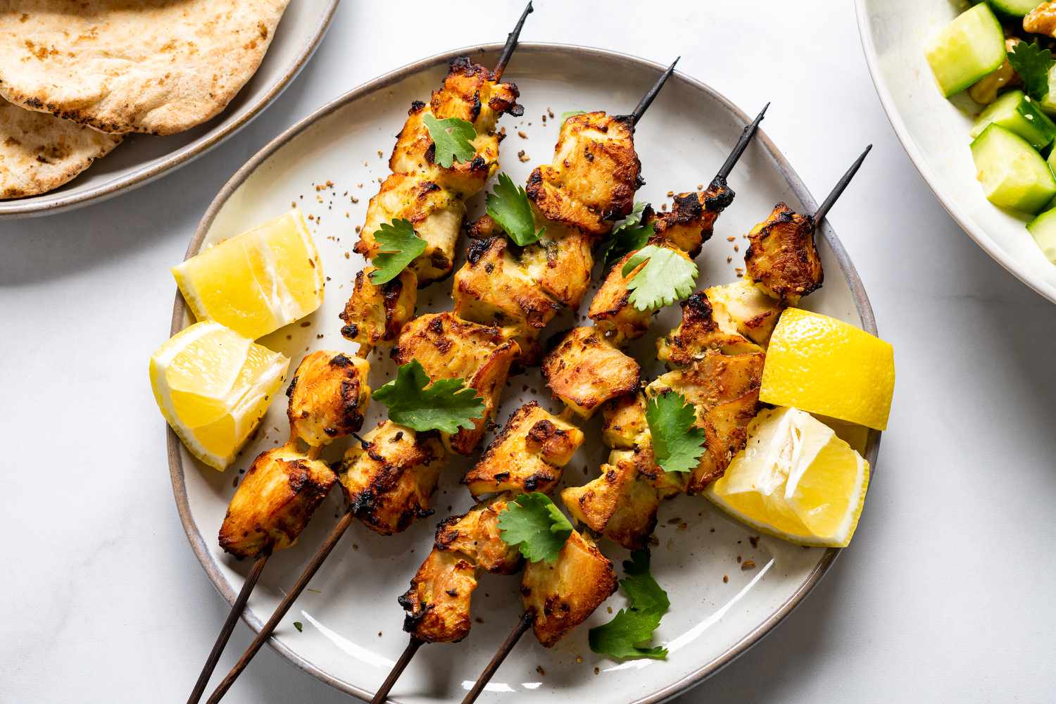 Bowls of Greek yogurt, spices, chopped chicken, lemon, garlic, and chopped onion and bell pepper arranged on a bright kitchen counter