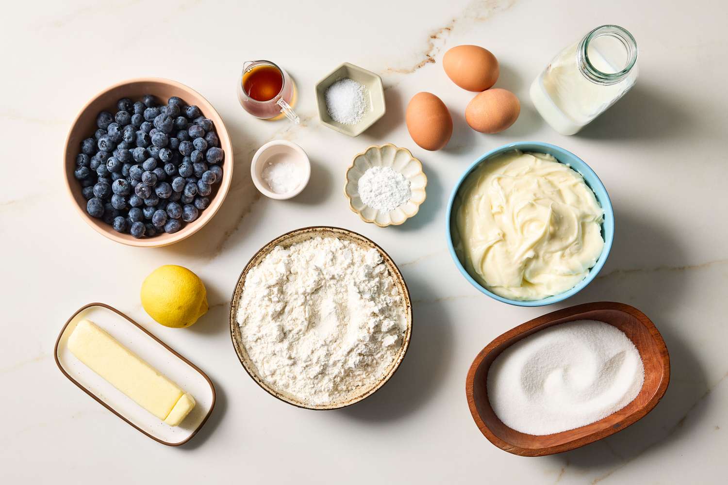 Bowls of cake flour, sugar, and butter with eggs, buttermilk, vanilla, and a small measuring cup of oil arranged on a bright kitchen counter, ready for baking
