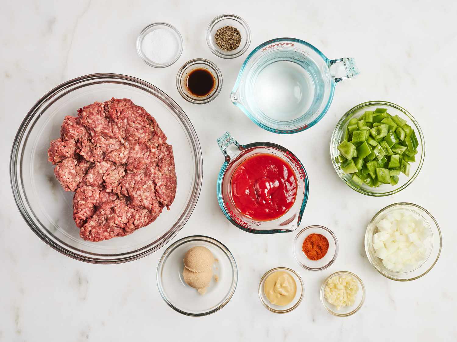 Bowls of dry brown lentils, diced onion, diced bell pepper, minced garlic, tomato sauce, and spices arranged on a neutral kitchen counter