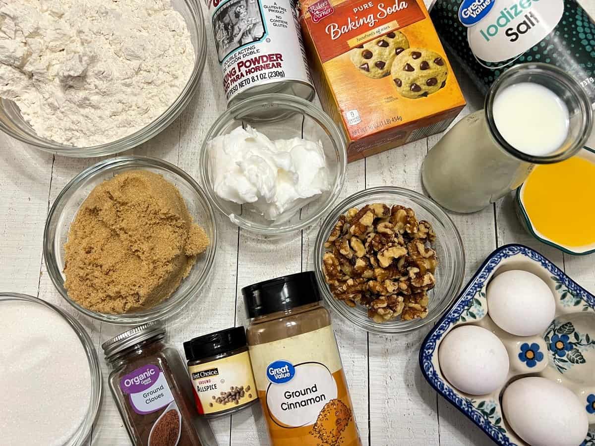 Bowls of flour, brown sugar, cinnamon, ginger, cloves, eggs, buttermilk, and oil arranged on a clean kitchen counter in natural light