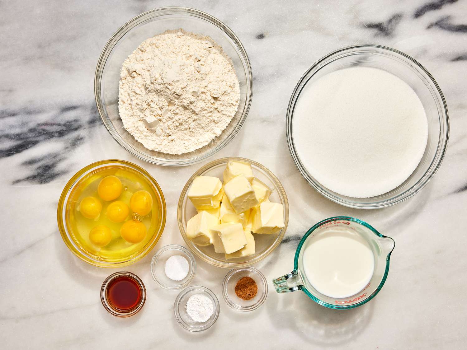 Bowls of flour, sugar, softened butter, cream cheese, eggs, vanilla, and a Bundt pan arranged on a clean kitchen counter in natural light