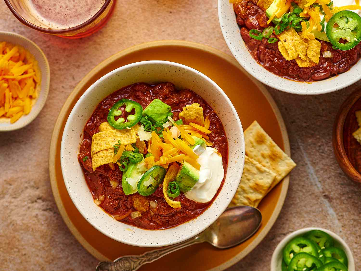 Bowls of ground beef, diced onion, minced garlic, canned beans, crushed tomatoes, and small dishes of chili spices arranged on a clean kitchen counter
