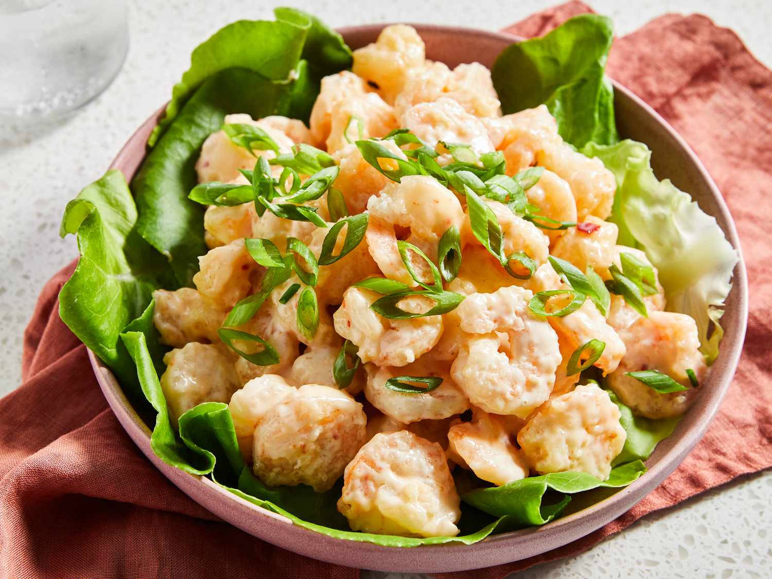 Bowls of raw peeled shrimp, mayonnaise, sweet chili sauce, sriracha, cornstarch, flour, eggs, and sliced scallions arranged on a tidy kitchen counter with warm lighting