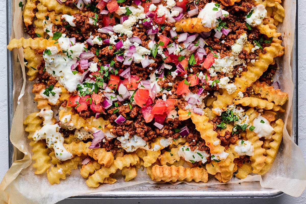 Bowls of shredded cheese, sour cream, lime, chopped onion, jalapeños, and a bag of frozen fries arranged on a kitchen counter