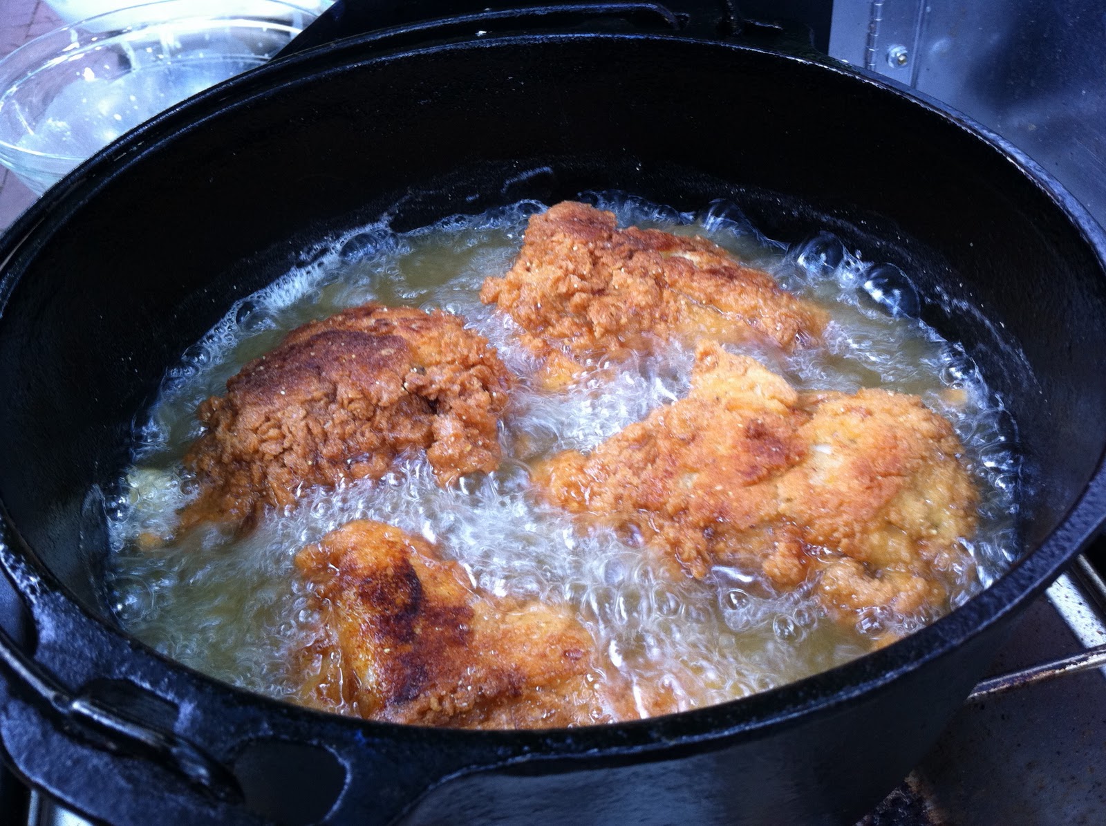Breaded chicken pieces frying in hot oil in a Dutch oven on a home stove with a thermometer clipped to the pot