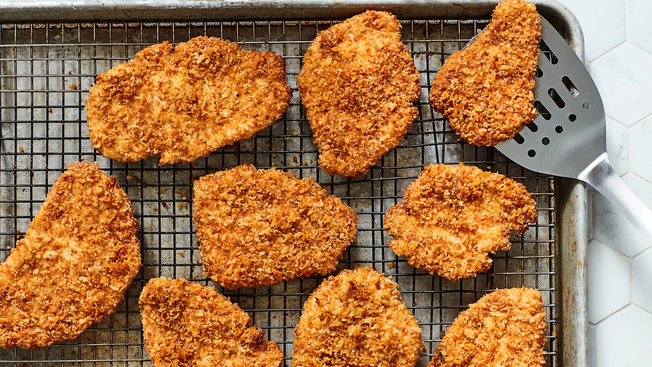Breaded chicken thigh pieces coated in panko on a sheet pan, sized to fit slider buns, ready to fry