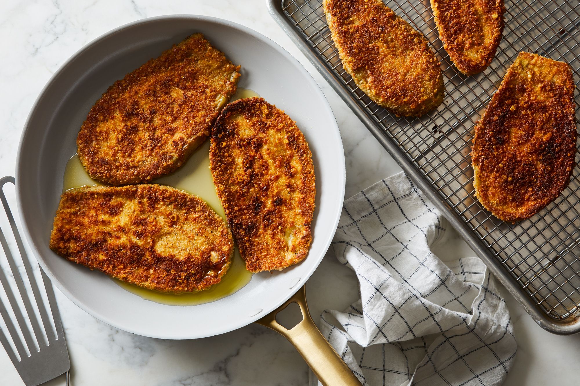 Breaded eggplant slices arranged in a single layer on a parchment-lined sheet pan, ready to fry