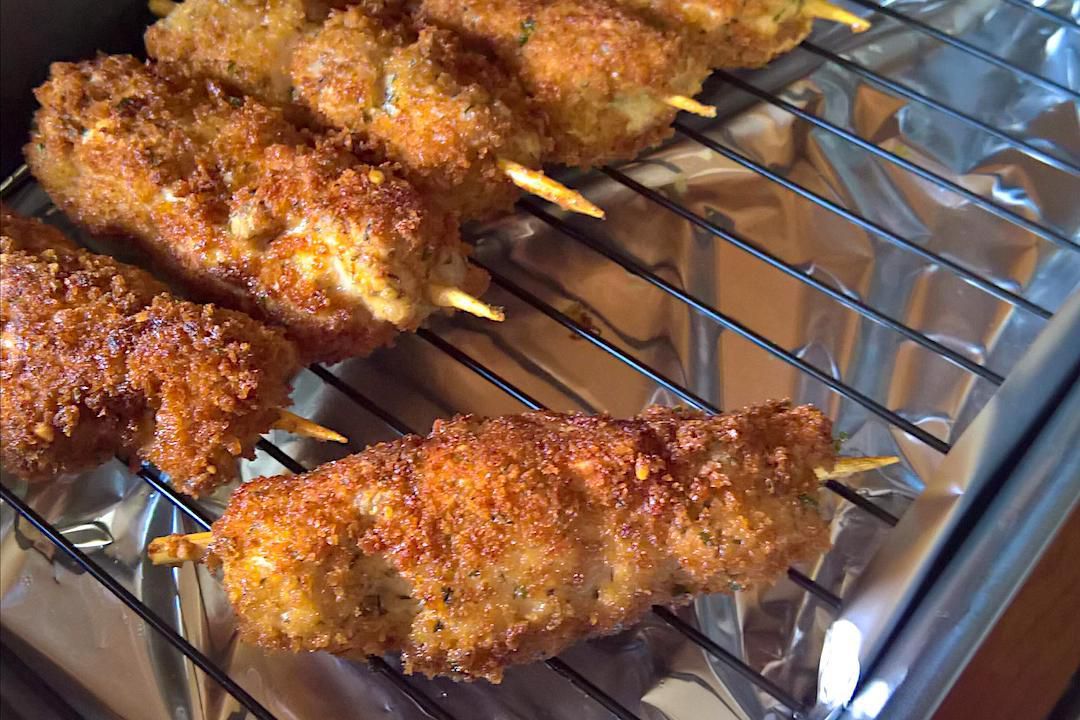 Breaded pork skewers sizzling and turning golden brown in a cast iron skillet on a stovetop