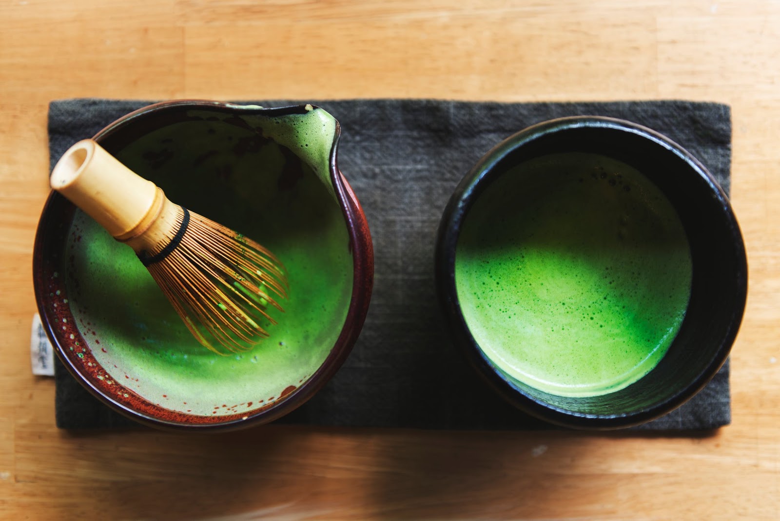 Bright green matcha being whisked with warm water in a small ceramic bowl on a kitchen counter
