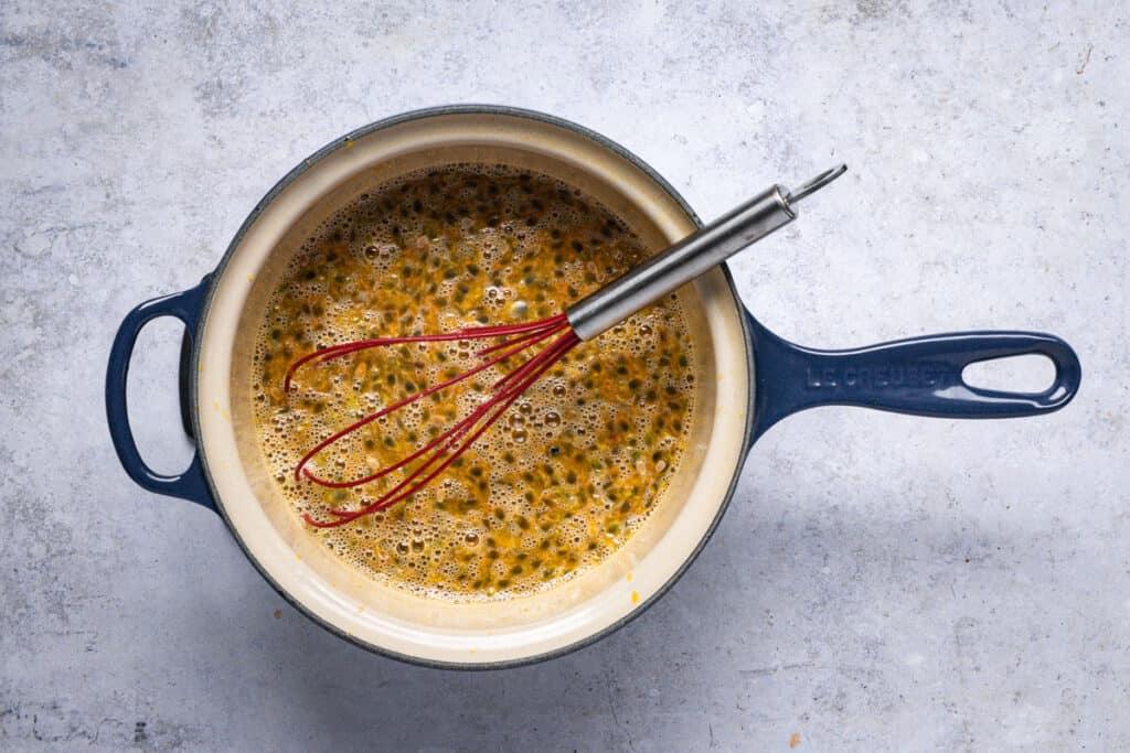 Bright yellow passion fruit curd thickening in a stainless steel saucepan on a stovetop